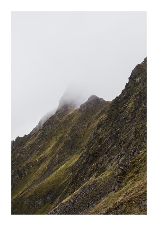 Farbbild im Hochkant Format mit weißem Rahmen zu sehen ist ein steiler Felsgrat der grün-gelb bewachsen ist von der Seite. Die uns Zugewandte Seite ist grün und direkt am Kamm verliert sich alles weitere in den Wolken.