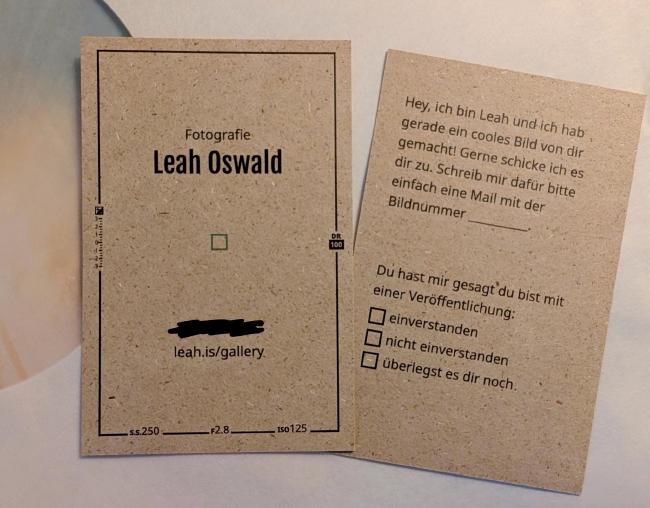 Zwei Visitenkarten nebeneinander. Einmal die Vorderseite und einmal die Rückseite. Auf der Vorderseite steht Fotografie und dann größer Leah Oswald. Darunter ein kleiner grüner Kasten in der Mitte der Karte der den scharf gestellten Autofokus symbolisiert. Im schwarzen Rahmen der Karte sind einige Werte wie S.S 250, F2.8 oder ISO 125 hinterlegt. Auf der Rückseite steht: Hey, ich bin Keah und hab gerade ein cooles Bild von dir gemacht! Gerne schicke ich es dir zu. Schreib mir dafür bitte einfach eine Mail mit der Bildnummer ____. Außerdem etwas weiter unten: Du hast mir gesagt, du bist mit einer Veröffentlichung und dann eine Auswahl zwischen 'einverstanden', 'nicht einverstanden' und 'überlegst es dir noch'