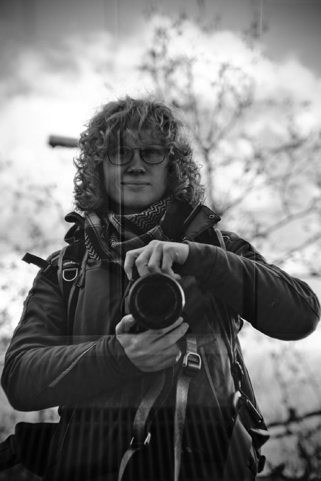 Leah Spiegelung in einer Scheibe mit der Kamera vor der Brust, sodass da Gesicht sichtbar ist.