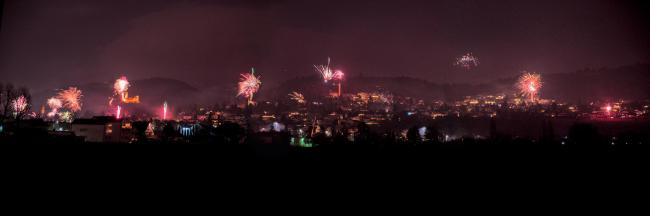 Panorama der Bergstraße bei Nacht. Der Vordergrund ist quasi schwarz. Im Hintergrund ist jede Menge Feuerwerk über der Bergstraße zu sehen die dadurch in einen roten Lichtschein getaucht ist.