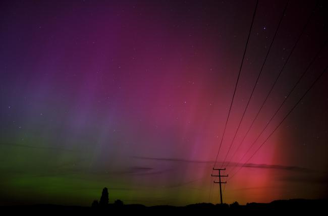 Es sind wellenartige rötlich über lila bis grüne Polarlichter zu sehen. Im Hintergrund liegt der Odenwald und den Vordergrund durchzieht ein Strommast mit seinen Leitungen