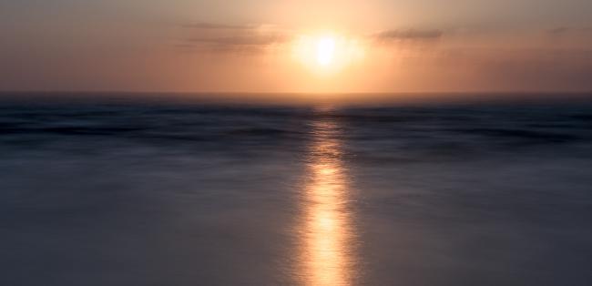 Farbbild in einem 2:1 Landscape Format. Das Bild ist vor allem im Horizont leicht unscharf bzw. verwackelt was dem ganzen einen etwas verträumten mysteriösen Anstrich gibt. Im oberen Drittel sieht man eine über dem mehr untergehende Sonne mit wenigen Wolken links und rechts von ihr. Das mehr selbst ist durch eine etwas längere Belichtung glatter und zeigt weniger Struktur. Trotz allem gibt es viele verschiedene Grau/Blau Töne und die Sonne spiegelt sich in einem langen Streifen bis zum unteren Bildrand. Die Sonne ist dabei leicht rechts von der Bildmitte.