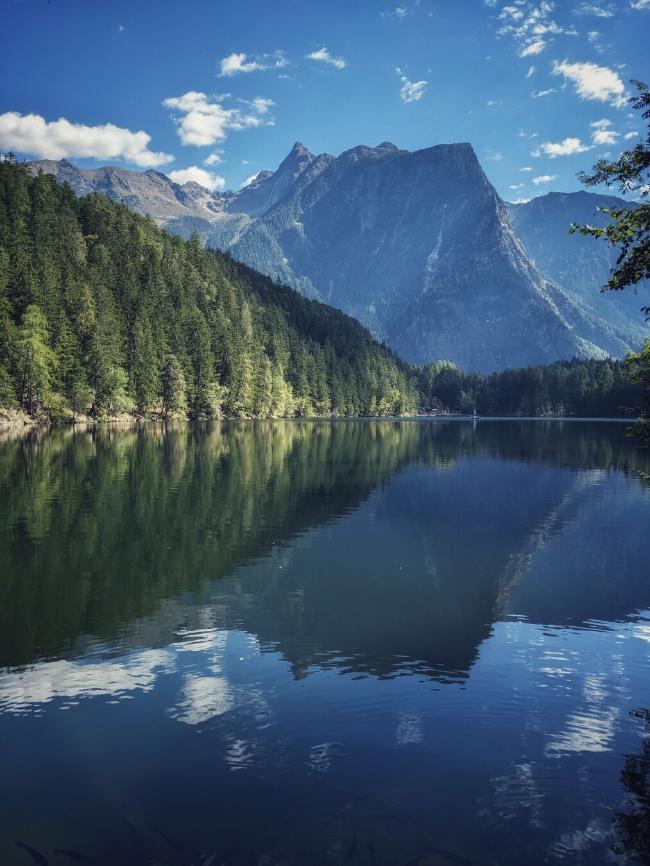 a lake with a beautiful mountain landscape behind it. It is sunny and there are only a few clouds on the blue sky