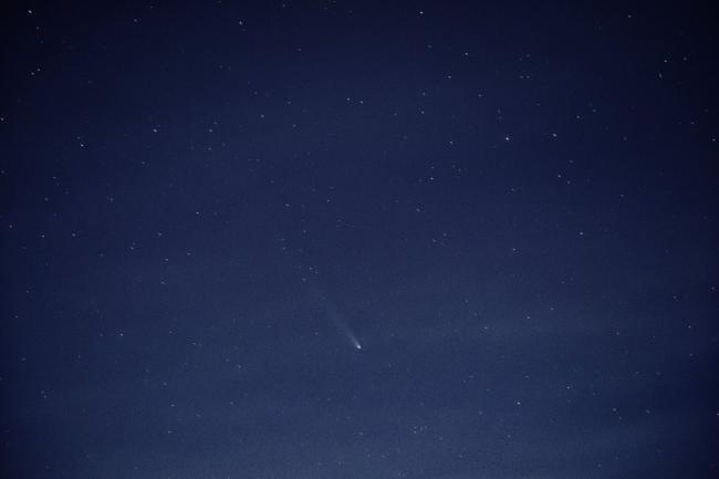 Bild eines blauen Sternenhimmels mit einem kleinen Komet leicht unterhalb der Mitte. Ist quasi ein heller Punkt mit einem Schweif.