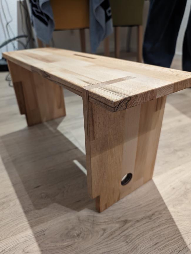 Holz-Ablage von der Seite. Man sieht die Kabeldurchführung an einem Bein und den Ausschnitt für die Fußleiste 