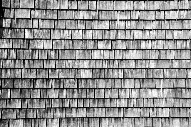 Schwarz-Weiß Bild der Holzfassade an einer Hütte in den Alpen. Sieht toll die Färbung und Struktur der Holzschindeln mit denen die Fassade der Hütte bedeckt ist.