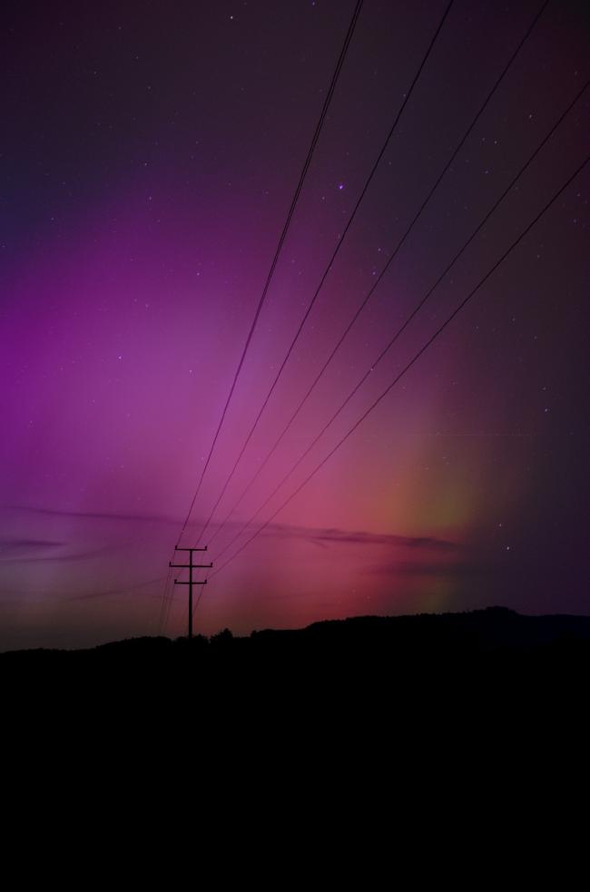 Hochtankaufnahme. Rote bis Lila Polarlichter mit einem Hauch grün und sichtbarer Struktur. Im Vordergrund ein Strommast und seine Leitungen