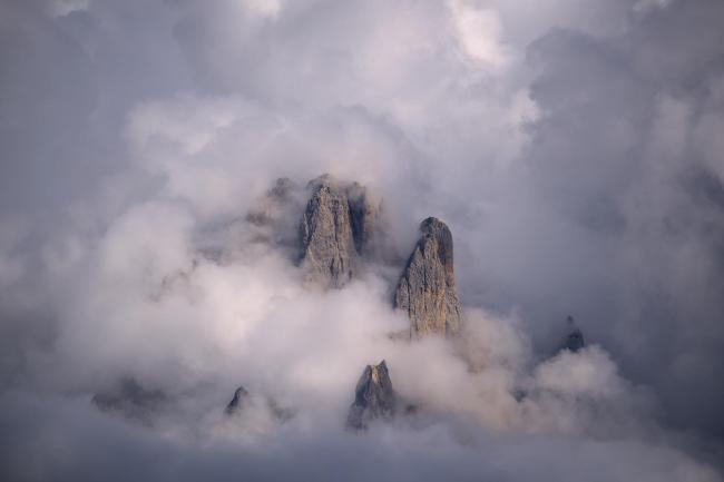 Farbbild im Landscape Format. Zu sehen sind zwischen dichten Wolken hervorbrechende und von der Sonne angestrahlte Teile des Langkofels.