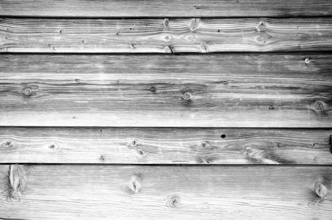 Schwarz-Weiß Bild der Holzfassade an einer Hütte in den Alpen. Man sieht sehr gut die Musterung und an verschiedenen Stellen die Astlöcher.