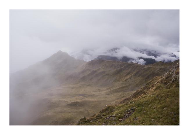 Farbbild im Querformat mit weißem Rahmen. Zu sehen ist eine Talkessel zwischen einem Berg und einem Kam in der Bildmitte. Der Nebel zieht gerade von Links ins karge Tal. Und ein paar Sekunden später war auch nichts mehr zu sehen.