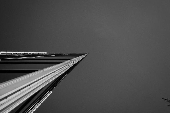Schwarz-Weiß Bild im Landscape Format. Aus der linken unteren Ecke ragt ein Gebäude spitz und keilförmig bis in die Bildmitte. Am rechten Rand sieht man zwei Zweige in das Bild ragen. Der eigentlich blaue wolkenlose Himmel ist hier auf dem Bild relativ gleichförmig grau.