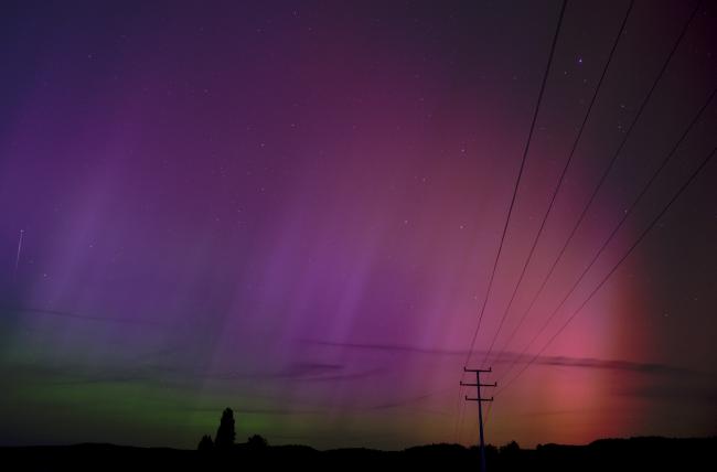 Es sind wellenartige rötlich über lila/blau bis grüne Polarlichter zu sehen. Im Hintergrund liegt der Odenwald und den Vordergrund durchzieht ein Strommast mit seinen Leitungen