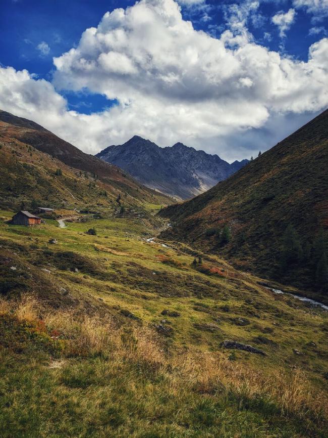 Blick in das hintere Horlachtal. Die Berghänge sind schon leicht herbstlich gefärbt und am blauen Himmel hängen große Wolken